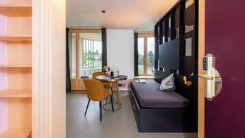 Ein modernes Zimmer mit einer Couch, einem kleinen Tisch und einem Sessel. Ein Fenster bietet Blick ins Freie.