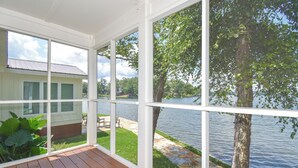 Una veranda riparata con ampie finestre che si affacciano su un lago e una zona verdeggiante con un edificio sullo sfondo.