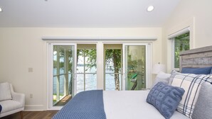 Una camera da letto con un letto grande, un divano e vista su un corpo d'acqua tramite porte di vetro.