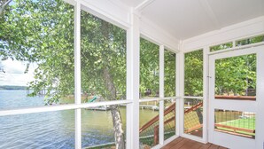 Una terrazza coperta con ampie finestre che si affacciano su un lago e una scala in legno che conduce a un'altra terrazza.
