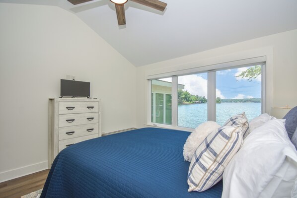 A bedroom with a large bed, a dresser, and a view of a lake through a sliding glass door.