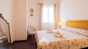 A bedroom with a bed, a chair, a nightstand, a lamp, and a mirror.