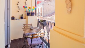 A balcony with a wooden table and chairs, potted plants, and a view of buildings in the background.