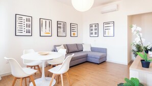 A modern living room with a gray sofa, white chairs, a round table, and framed abstract art on the wall. - Sa Perda e Su Entu - Morada (Iglesias)