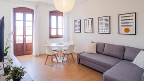 A modern living room with a gray sofa, a round dining table with chairs, and a large window with curtains. - Sa Perda e Su Entu - Morada (Iglesias)