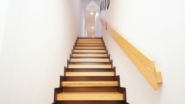 A wooden staircase with a handrail on the right side, leading to a landing with a geometric wall design. - Sa Perda e Su Entu - Morada (Iglesias)