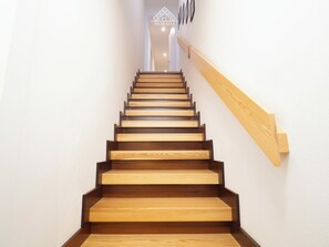 Een houten trap met een leuning aan de rechterkant, die uitkomt op een plateau met een geometrisch wandontwerp.