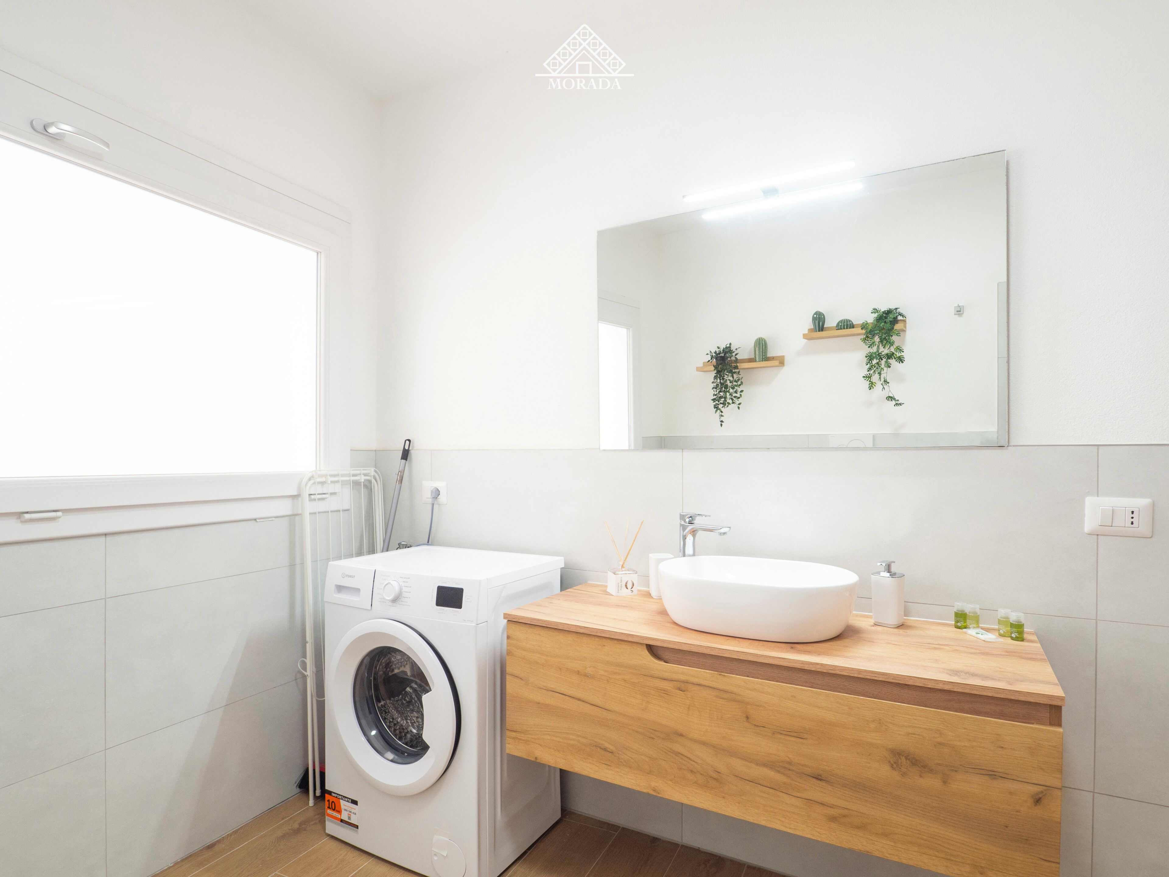 A modern bathroom with a washing machine, a sink, and a mirror.