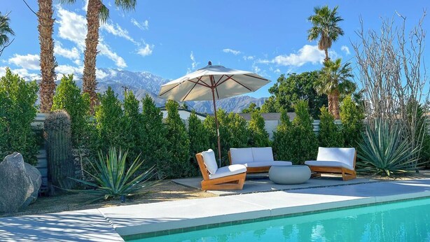 Zona de piscina con sillas de descanso y una sombrilla, rodeada de plantas tropicales y vistas a la montaña.