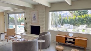 Una sala de estar moderna con chimenea, asientos cómodos, una mesa de centro y vistas a una piscina y zonas verdes.