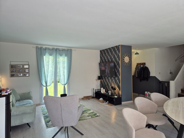 A modern living room with a grey armchair, a round table, and a TV mounted on a geometric-patterned wall. - House with swimming pool, pets welcome. 3300-metre fenced park (La chapelle montbrandeix)