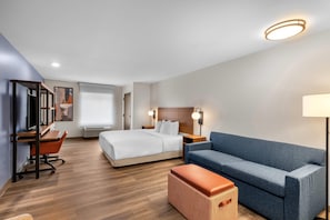 Une chambre d’hôtel moderne avec un lit, un canapé bleu, un bureau en bois et une lampe.