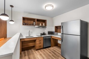 A modern kitchen with a stainless steel refrigerator, built-in microwave, and wooden cabinetry. - Everhome Suites Stockbridge Atlanta (Stockbridge)