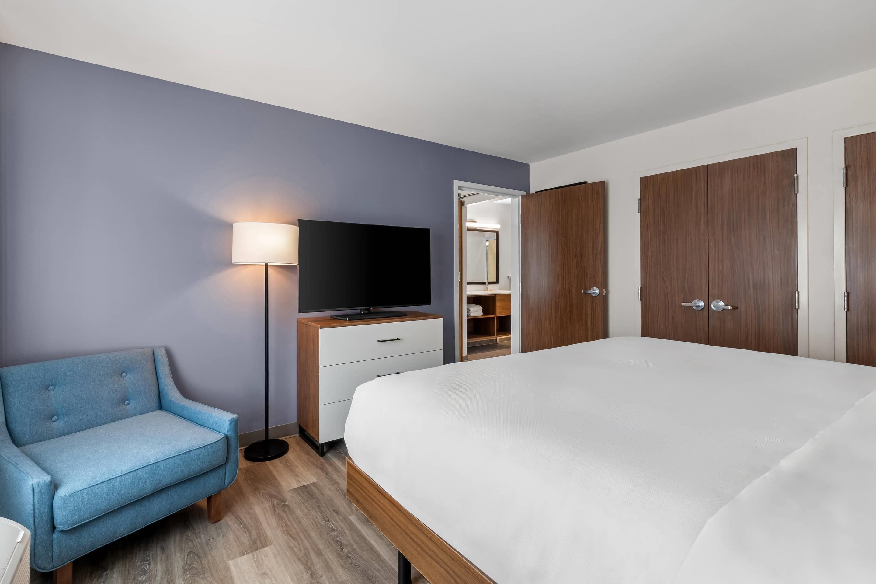 A bedroom with a bed, a TV, a sofa, and wooden wardrobes.