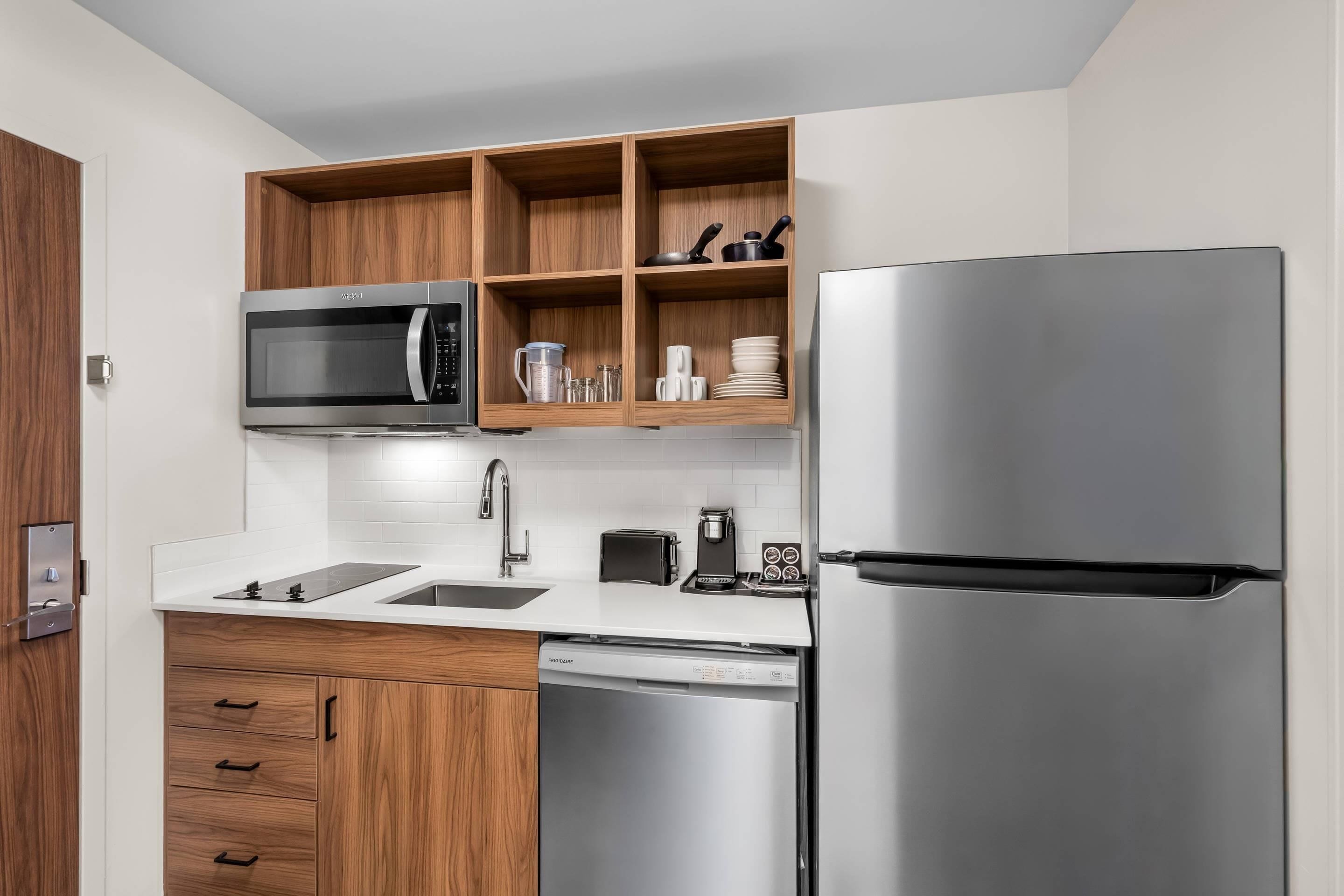 A modern kitchen with a stainless steel refrigerator, microwave, and dishwasher, wooden cabinets, and a white countertop.