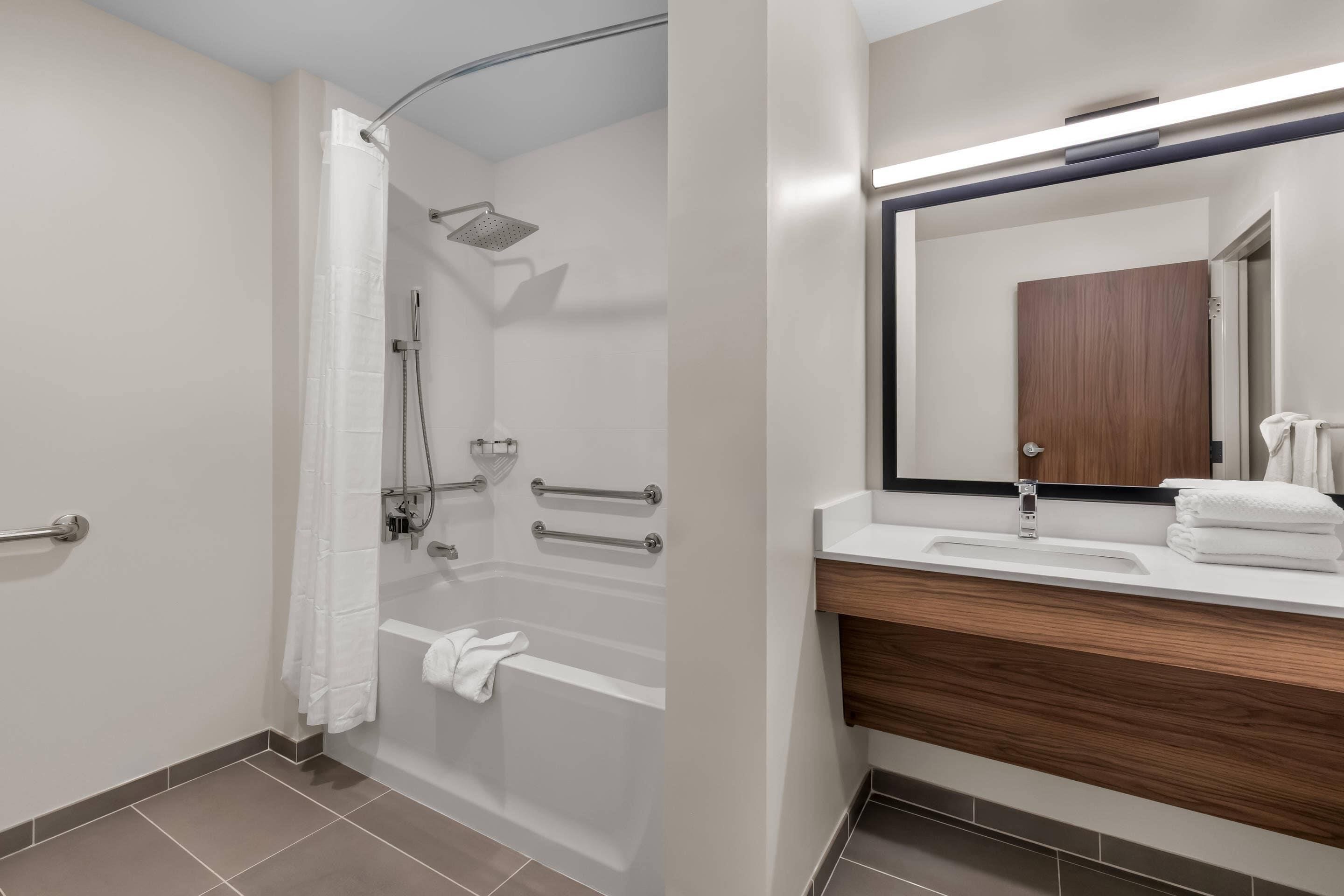 Un baño moderno con ducha, tocador con espejo y toallero.