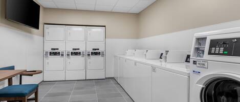 A laundry room with a washing machine, dryers, a table, and chairs.