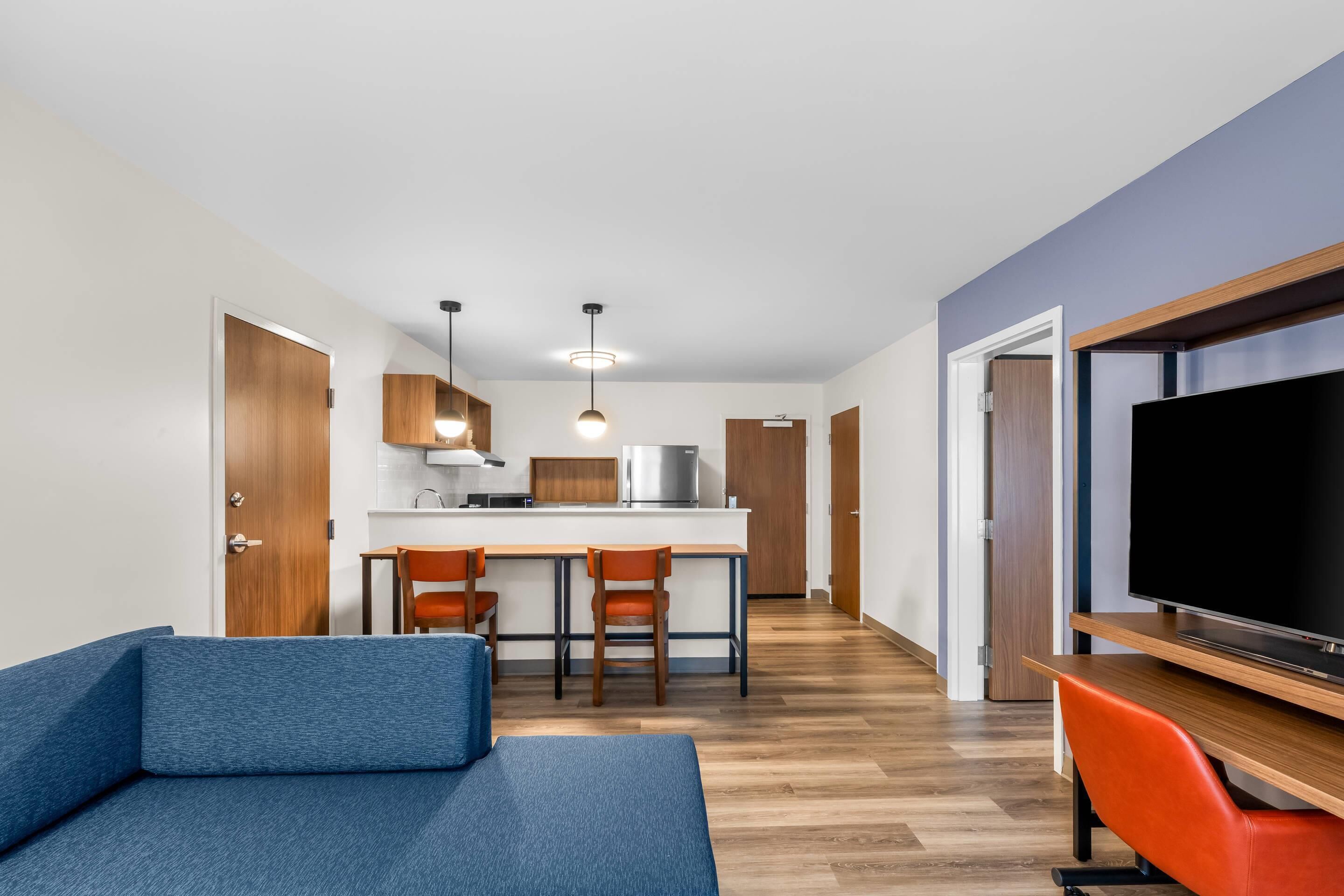 A modern living room with a sofa, a TV, and a kitchen area with a dining table and chairs.