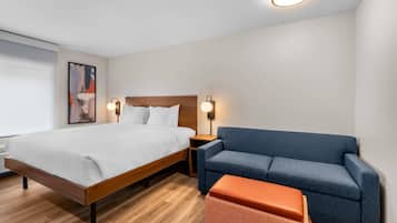 Habitación de hotel con cama, sofá azul, pequeño taburete naranja y dos lámparas fijadas a la pared.