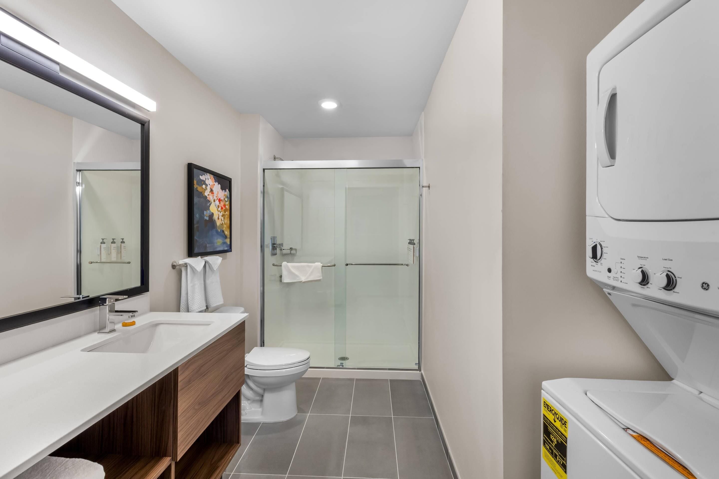 A modern bathroom with a glass shower enclosure, a white toilet, and a double sink vanity.