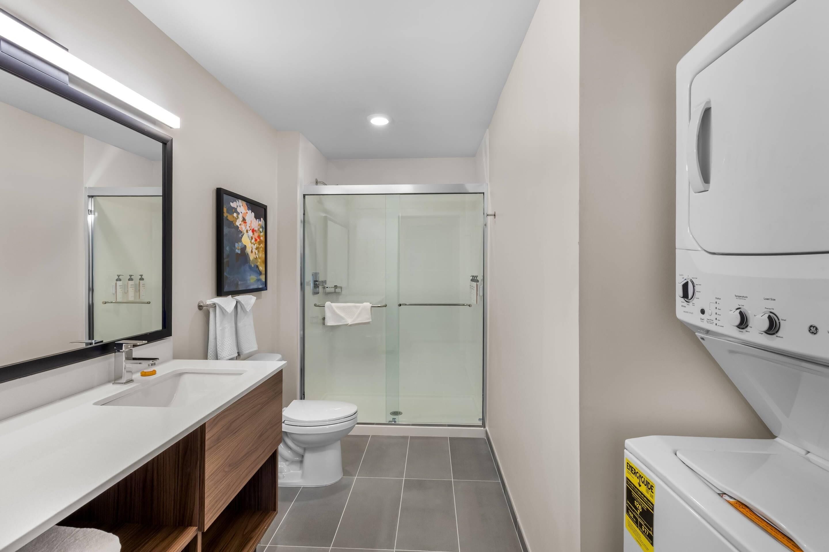 A modern bathroom with a glass shower enclosure, a white toilet, and a built-in washing machine.
