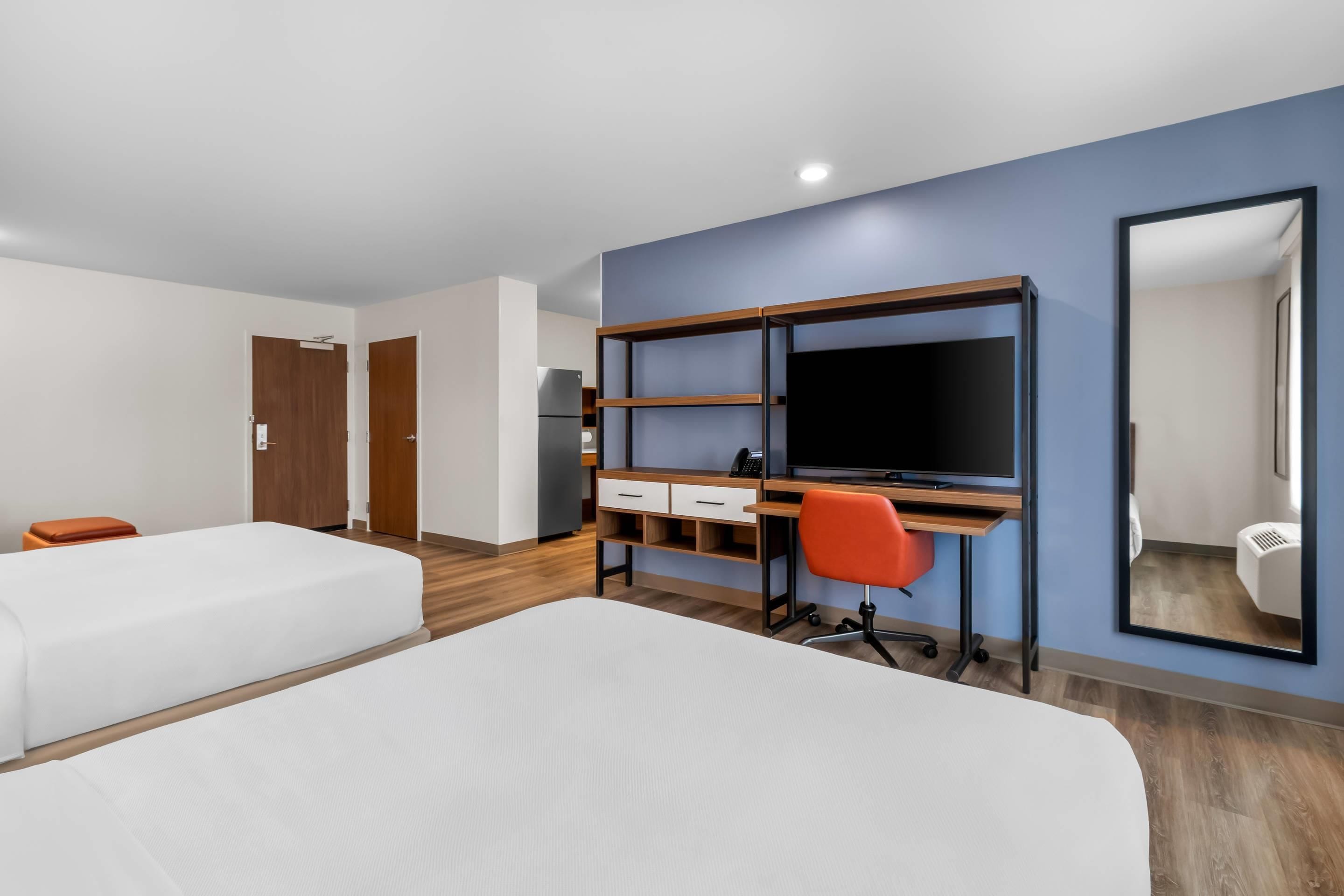 Une chambre d’hôtel avec deux lits, un bureau avec un ordinateur, une chaise et un grand miroir.