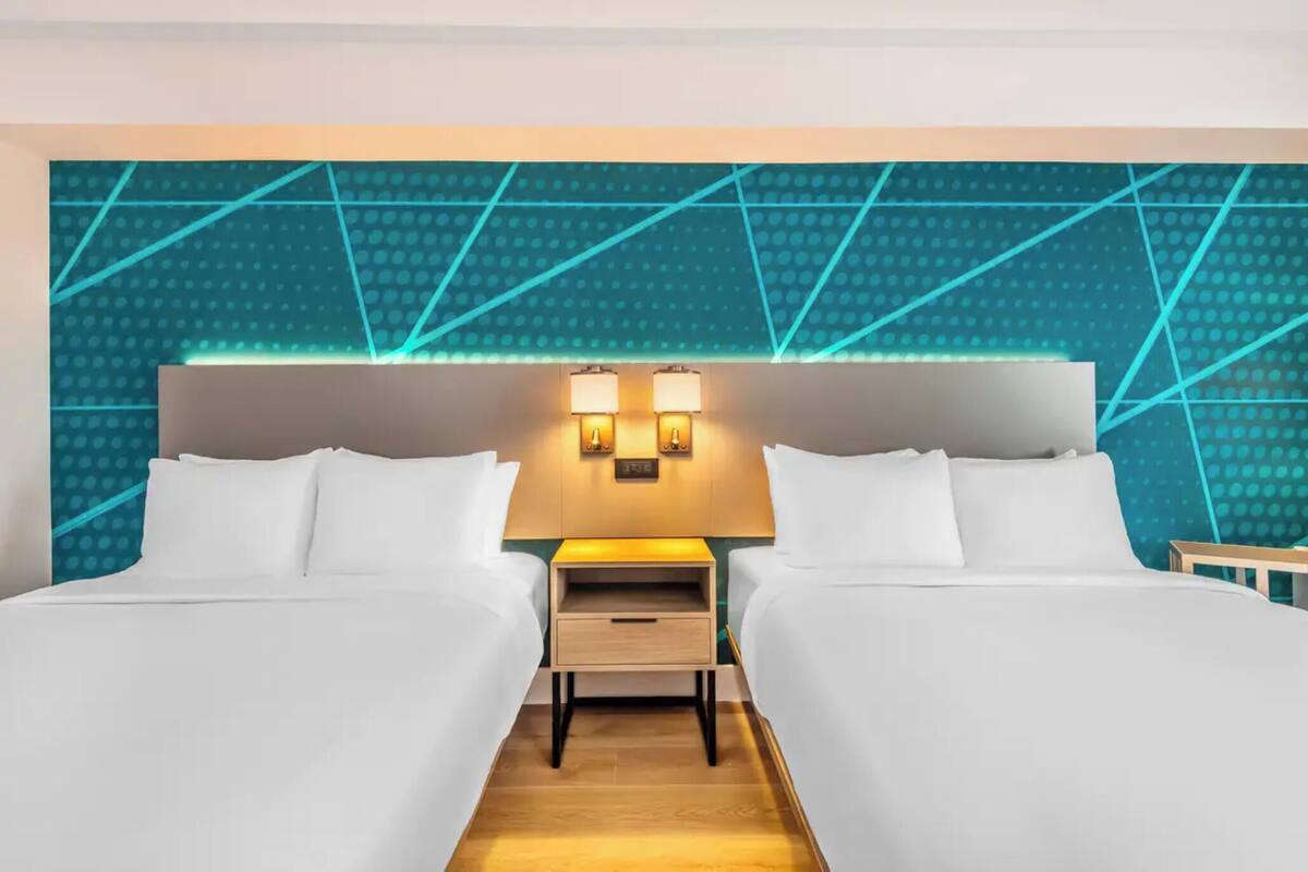 A hotel room with two beds, a nightstand with a lamp, and a geometric-patterned wall.