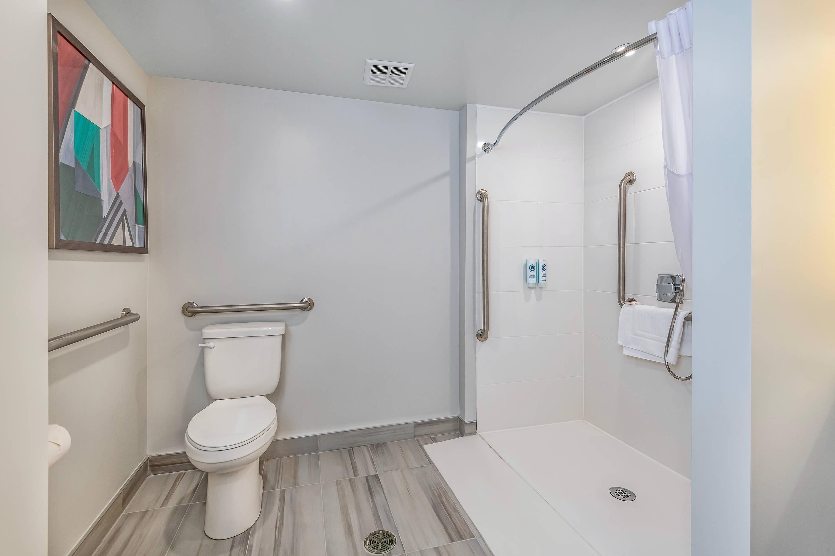 Une salle de bain moderne équipée de toilettes, d’une douche et de barres d’appui.