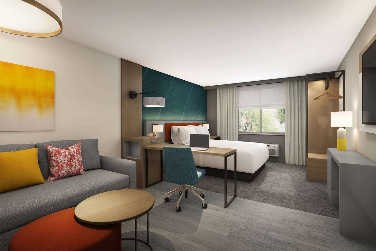 A modern hotel room with a sofa, a desk, a bed, and a small table.