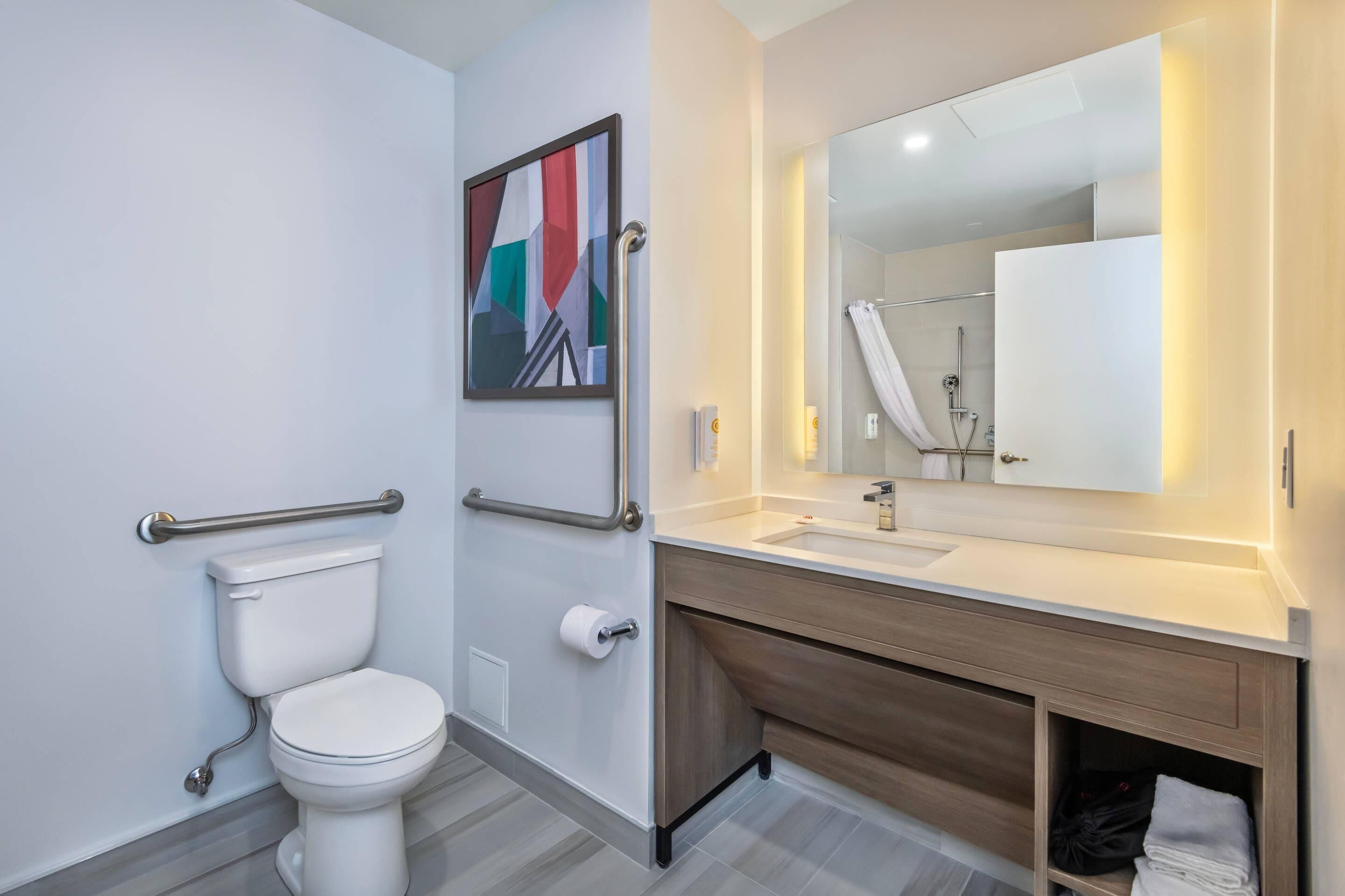 A modern bathroom with a toilet, handrails, a sink, and a mirror.