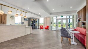 A modern hotel lobby with wooden flooring, a reception desk, red and grey seating, and large windows offering a view of the outdoors. - Comfort Inn & Suites (Cochrane)