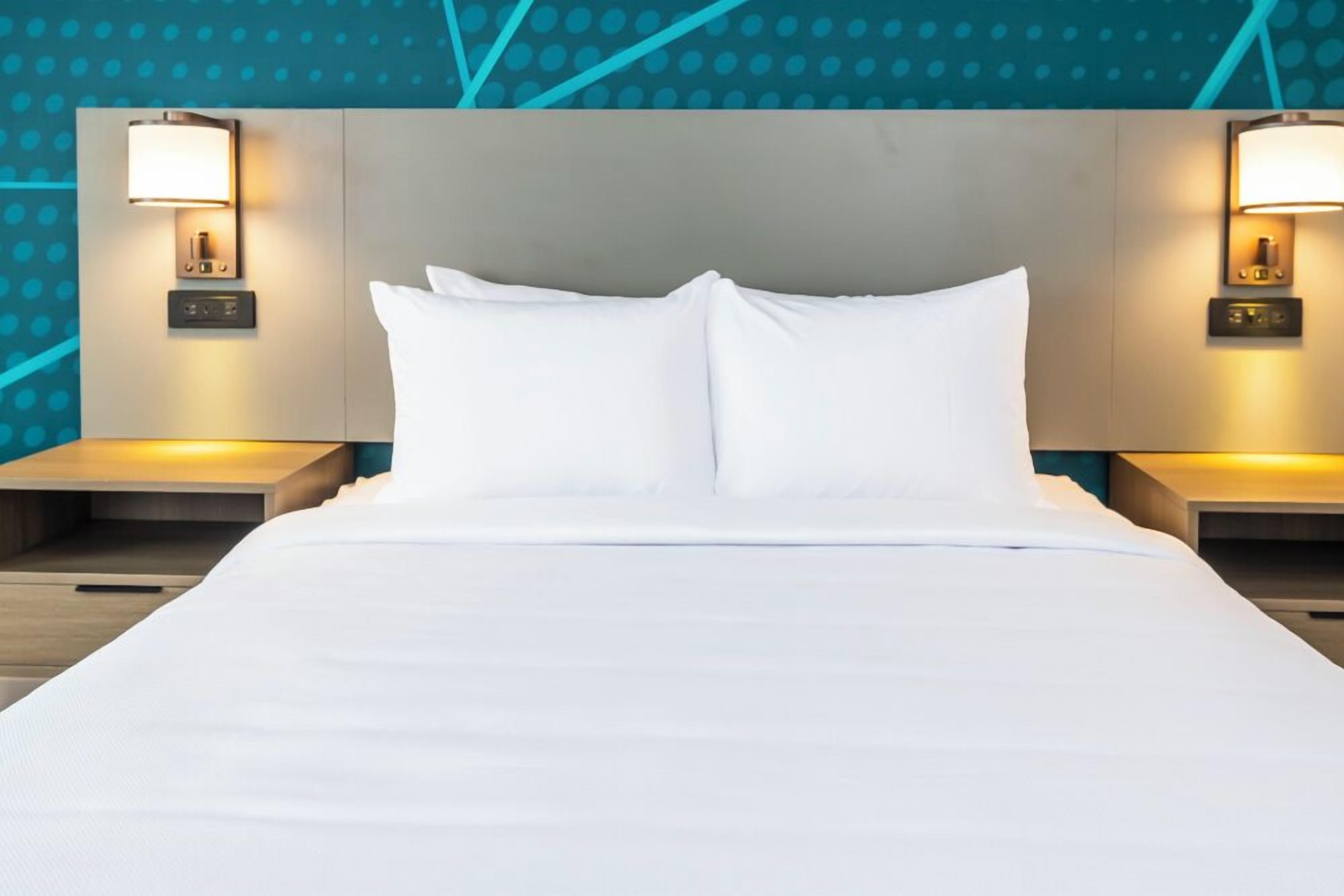 A hotel room with a large bed, two bedside tables, and wall-mounted lamps.