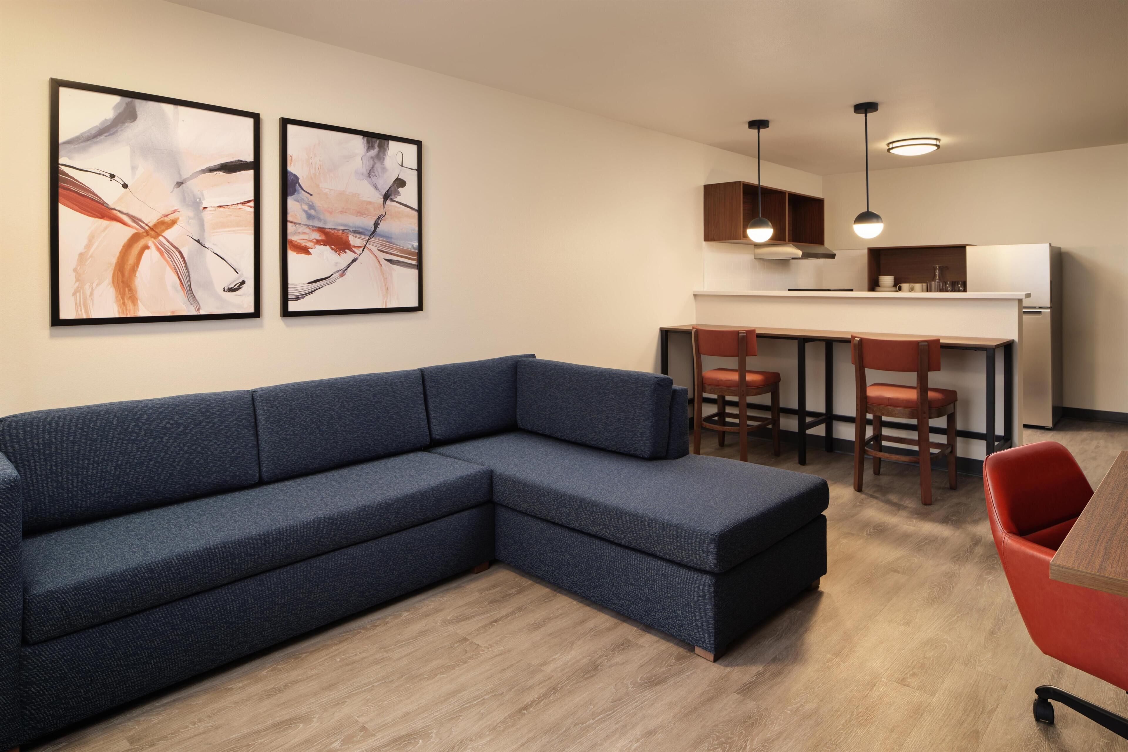A modern living room with a sectional sofa, a dining area with chairs, and abstract art on the wall.