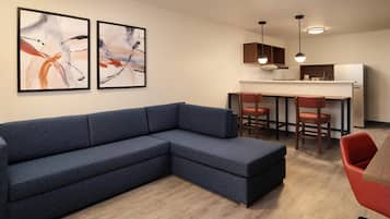 A modern living room with a sectional sofa, a dining area with chairs, and abstract art on the wall.
