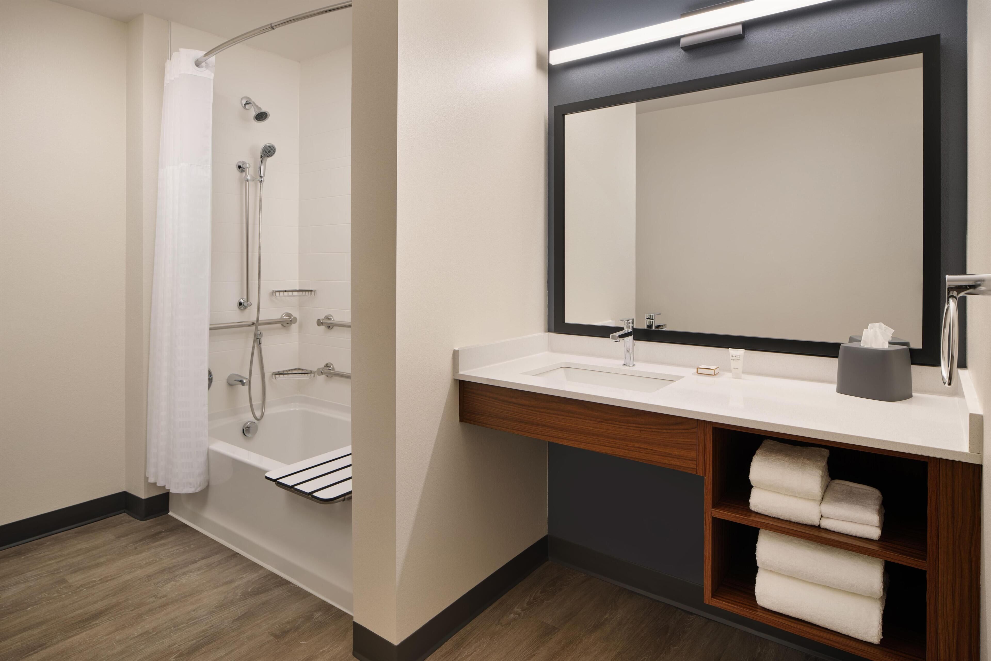 A modern bathroom with a bathtub, a sink, a mirror, and a towel rack.