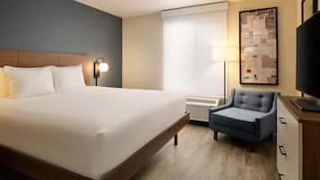 Une chambre d’hôtel avec un grand lit, une chaise, un bureau, une lampe, une télévision et une fenêtre avec des stores.