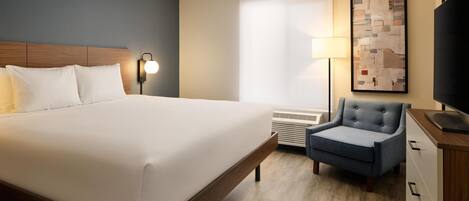 Habitación de hotel con una cama grande, una silla, un escritorio, una lámpara, un televisor y una ventana con persianas.