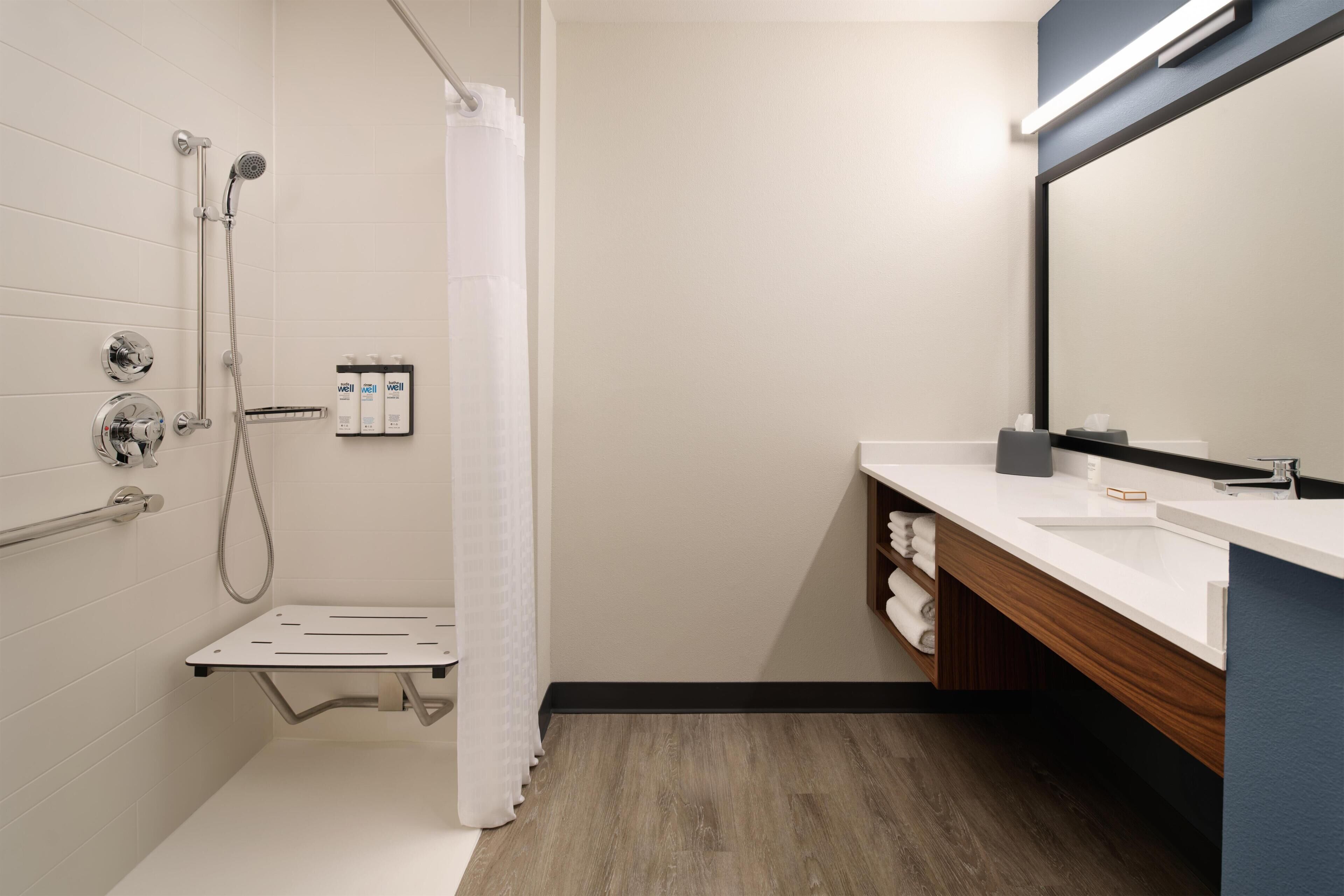 Un baño moderno con ducha, lavamanos, espejo y toallero.