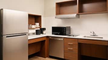 Una cocina moderna con un refrigerador de acero inoxidable, microondas, lavavajillas, armarios de madera y encimera blanca.