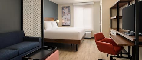 Una habitación de hotel con cama, escritorio, silla, sofá y televisor.