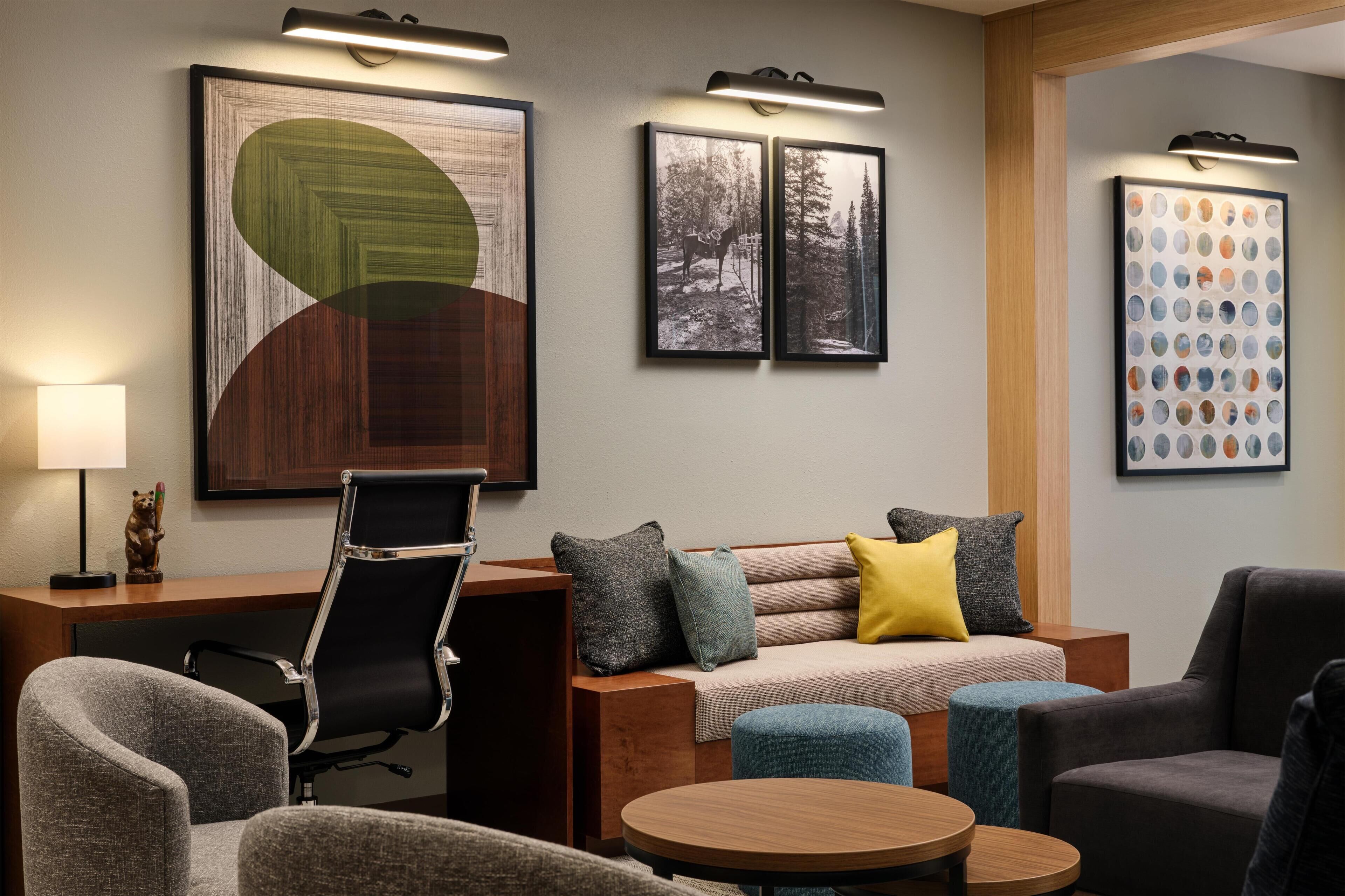A modern hotel room with a sofa, armchairs, a desk, and a round table.