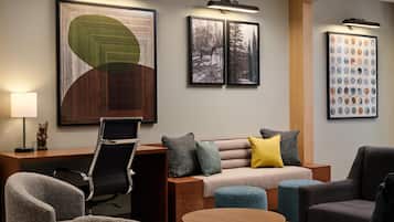 A modern hotel room with a sofa, armchairs, a desk, and a round table.