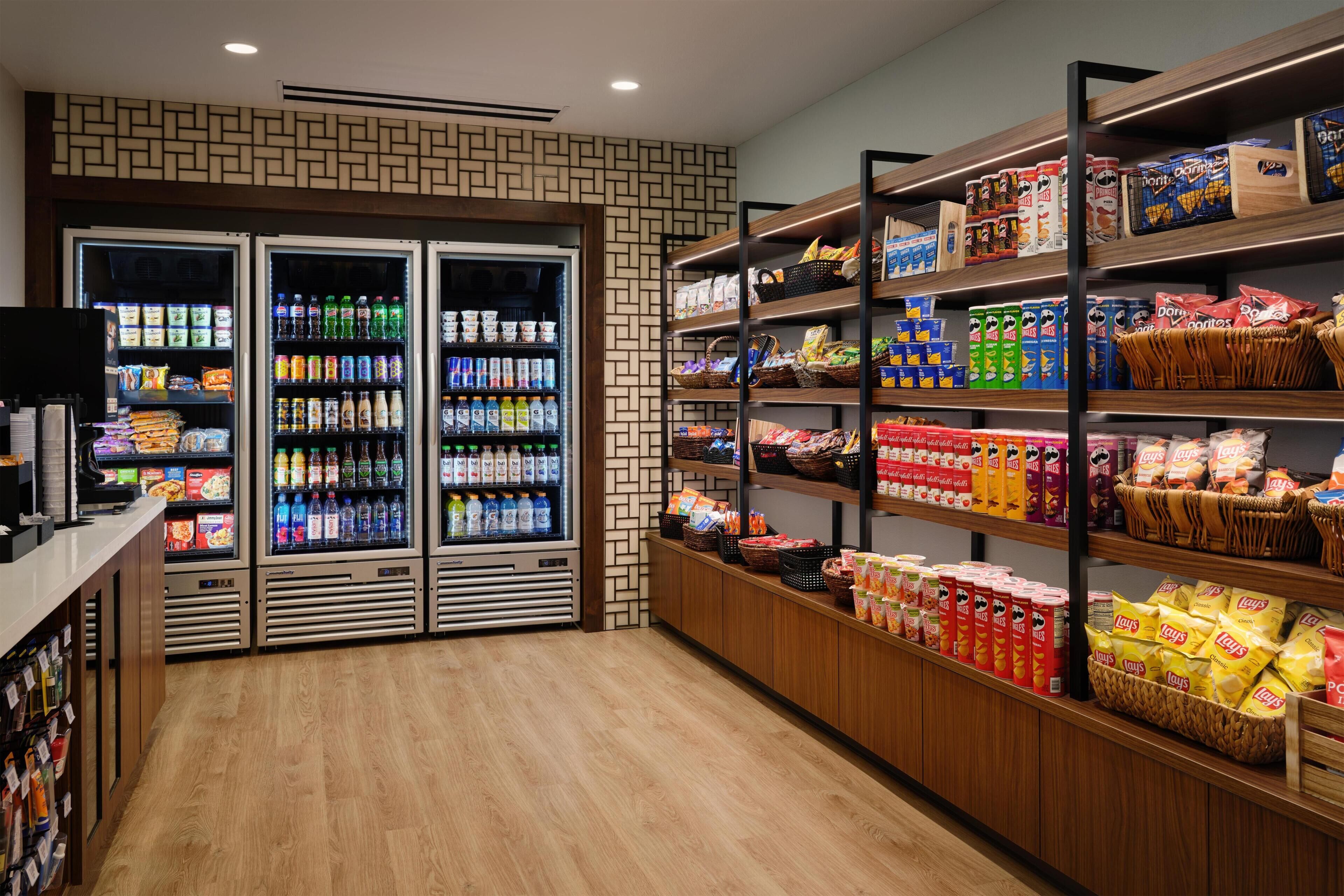 Interior de un supermercado con secciones refrigeradas, estantes llenos de productos de snack y piso de madera.