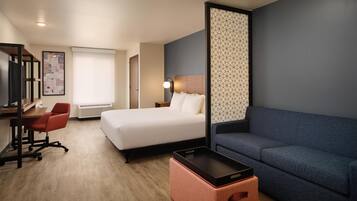 A hotel room with a bed, a desk with a chair, a sofa, a small table, and a partition wall.