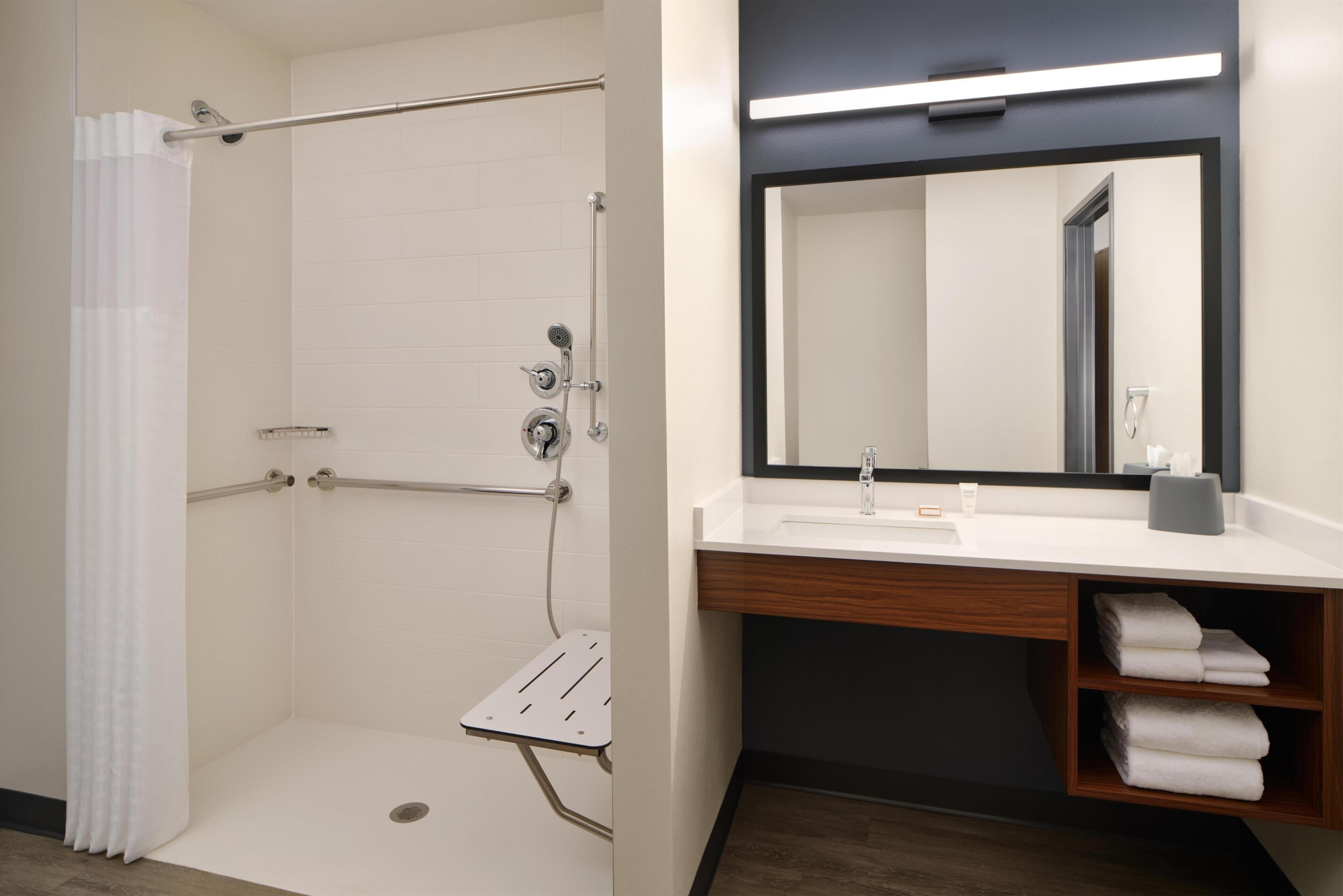 A bathroom with a shower, a sink, a mirror, and a towel rack.