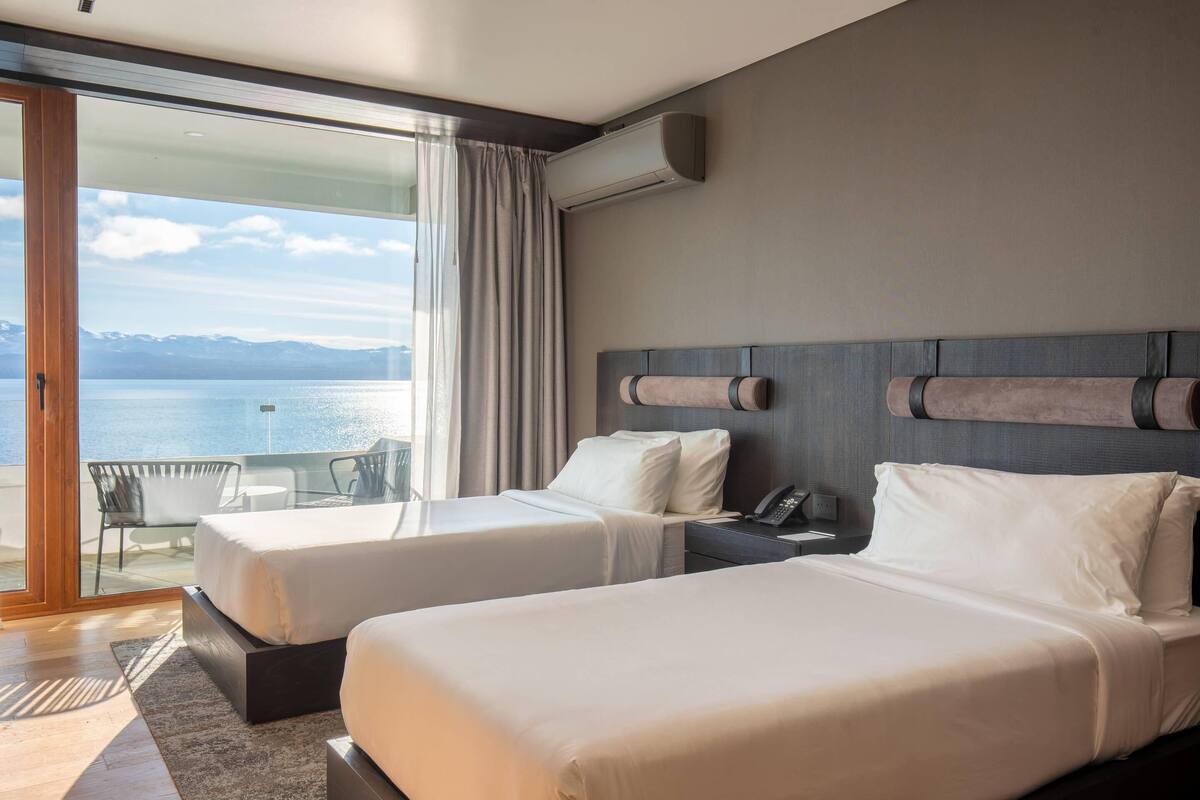 Ein Hotelzimmer mit zwei Betten, einem großen Fenster mit Meerblick und einer Klimaanlage an der Wand.