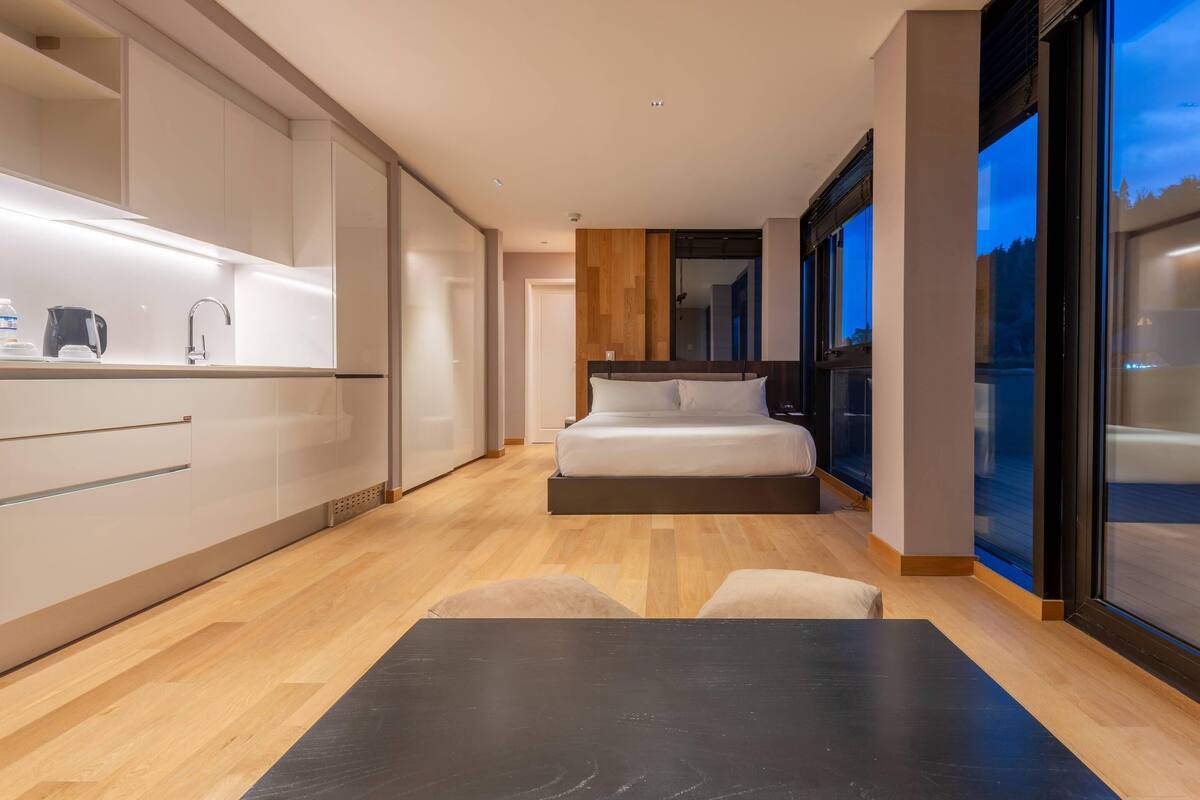 Ein modernes Schlafzimmer mit Bett, kleinem Tisch und einer Küchenzeile mit Schränken und Arbeitsplatte.