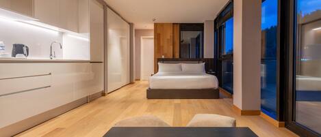 Un dormitorio moderno con cama, una mesita pequeña y una zona de cocina con armarios y encimera.