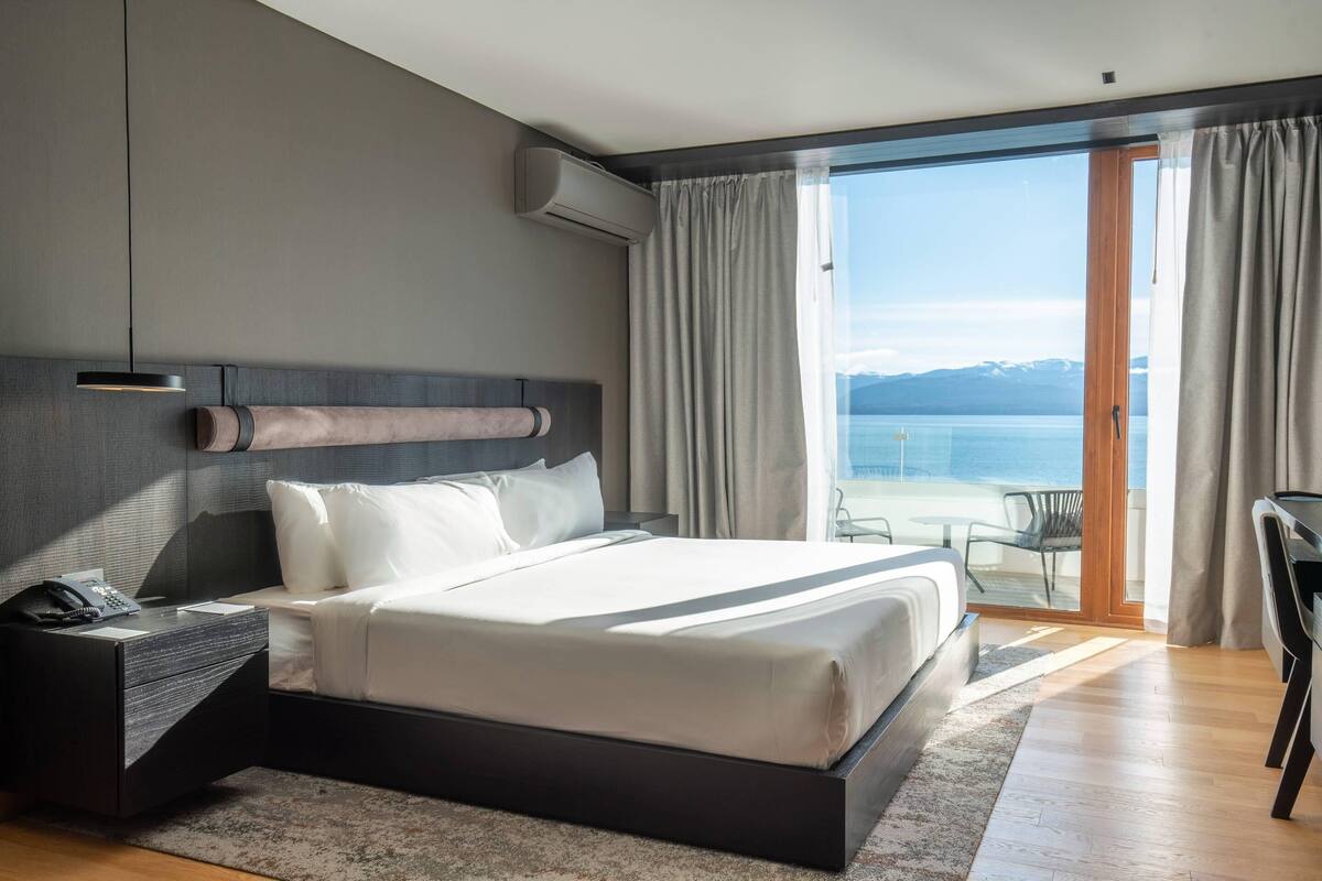 Ein modernes Hotelzimmer mit einem großen Bett, einem Schreibtisch und Blick auf das Meer.