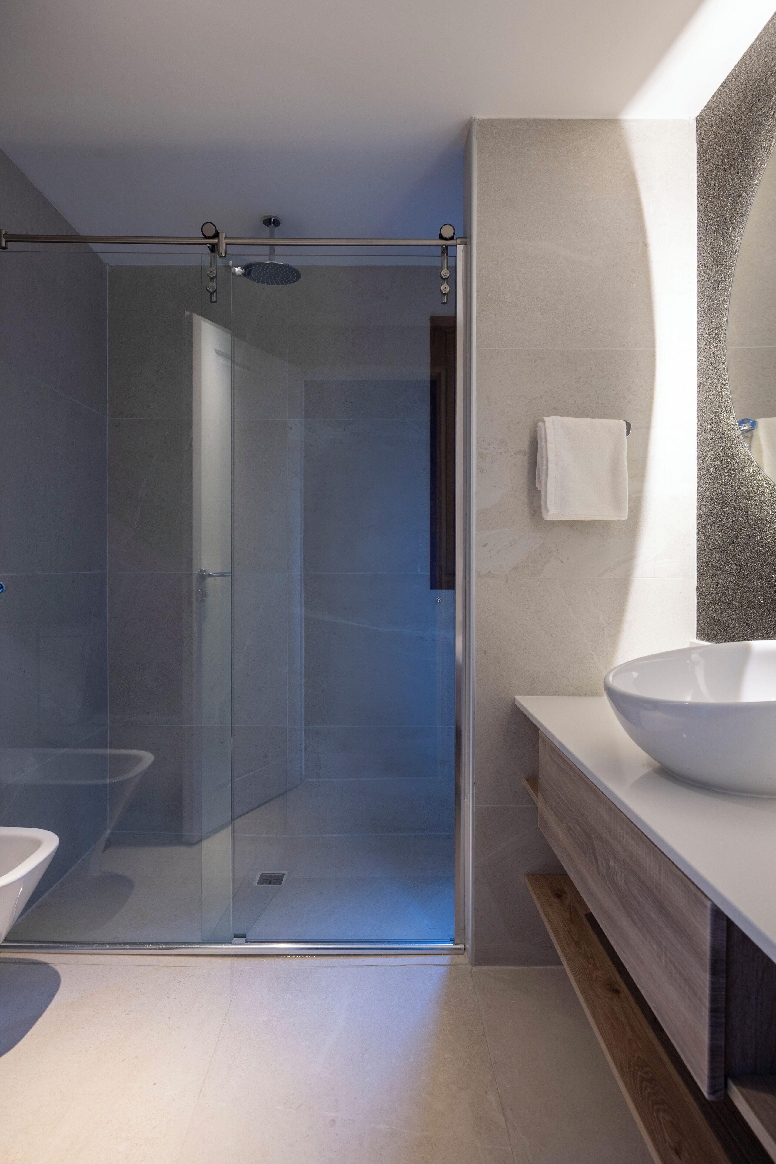 Un baño moderno con ducha de vidrio, un lavamanos grande y un espejo con pared texturizada.